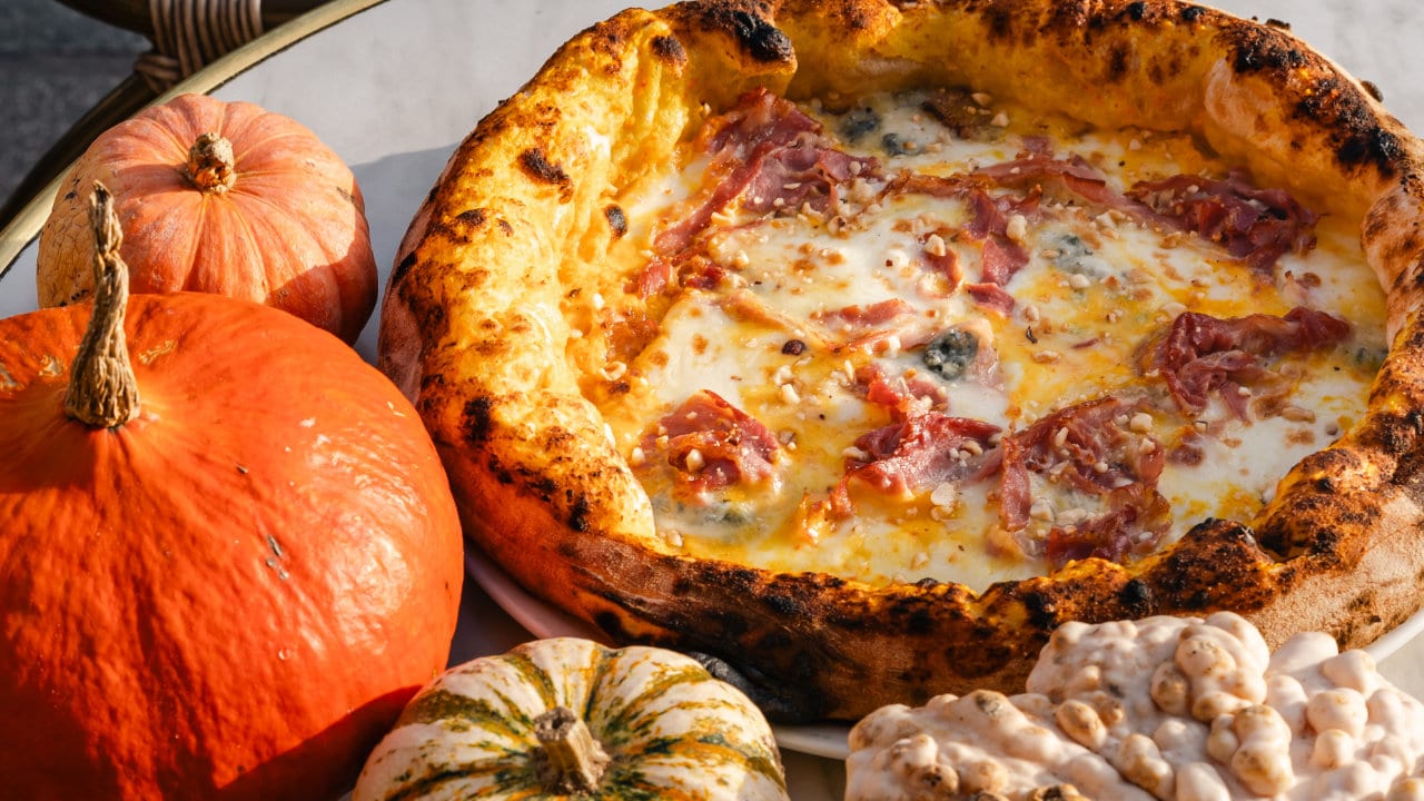 Pizza Zucca avec crème de potimarron, mozzarella, gorgonzola, pancetta et noisettes concassées, photographiée avec des courges aux Grandes Halles du Vieux-Port à Marseille.